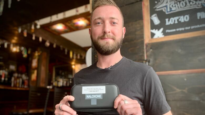 A man holds a black naloxone kit at a pub table