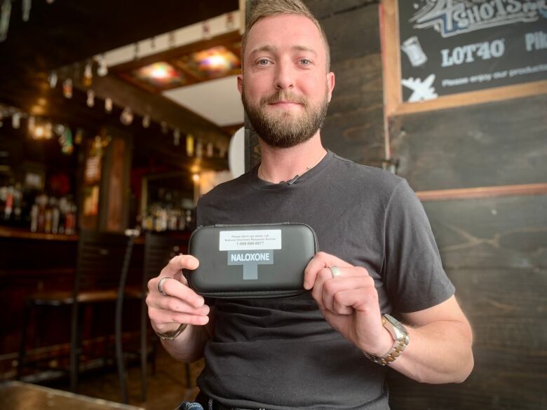 A man holds a black naloxone kit at a pub table