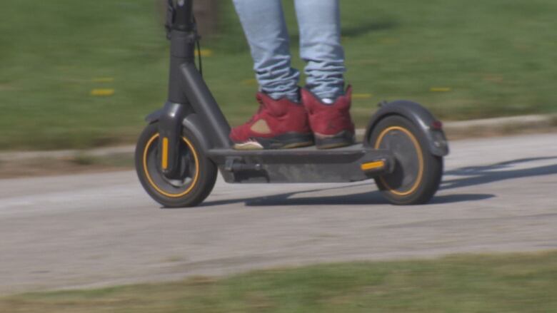 A man wearing red shoes rides an e-scooter