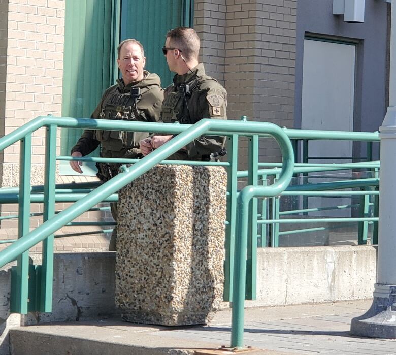 Two RCMP officers in camouflage talk to each other as they walk down a concrete ramp outside the Prince George courthouse. 