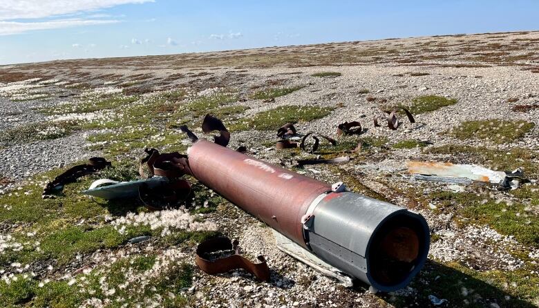 A rocket section and metal debris sits on the tundra.