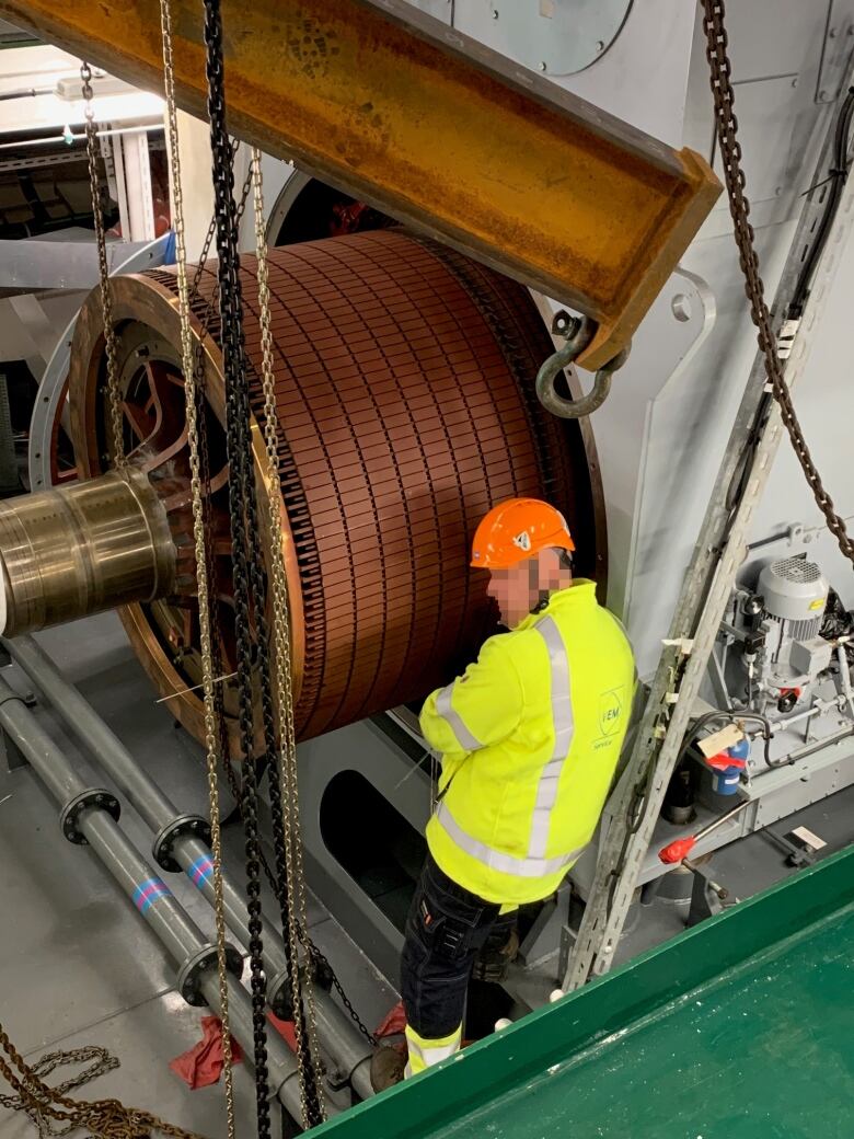 A large round motor is pictured with a working man standing beside it. 