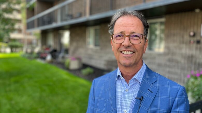 A man in a blue suit and glasses stands in front of a rental building in downtown Calgary.