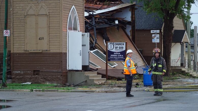 Two fire fighters stand next to a church that has been badly damaged by a fire. 