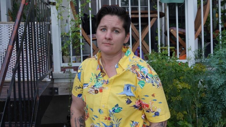 A woman wearing a yellow short-sleeve shirt stands beside stair railings. 