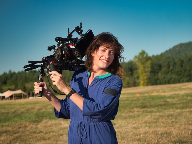 A portrait of a woman carrying a video camera in a field.