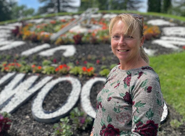 A woman with blond hair wearing a floral long-sleeved shirt standing in a park