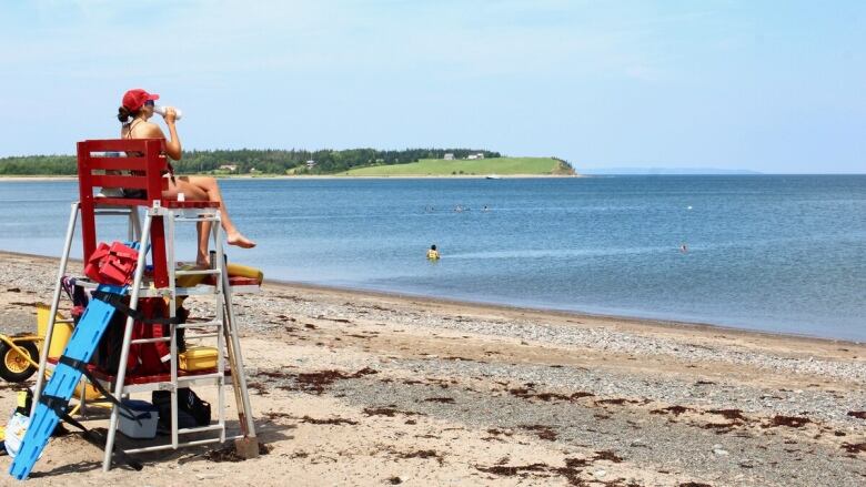 A lifeguard is seen sitting on a tower on a sandy beach, overlooking the water.