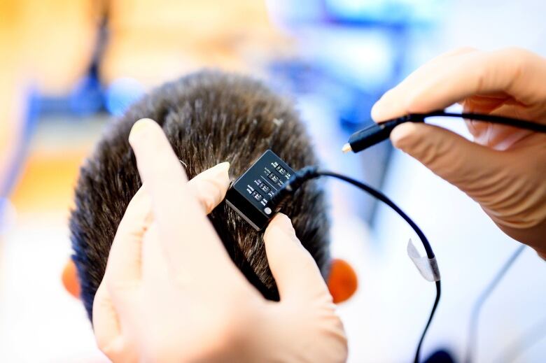 A person plugs wires into a box that sits on a person's head. 