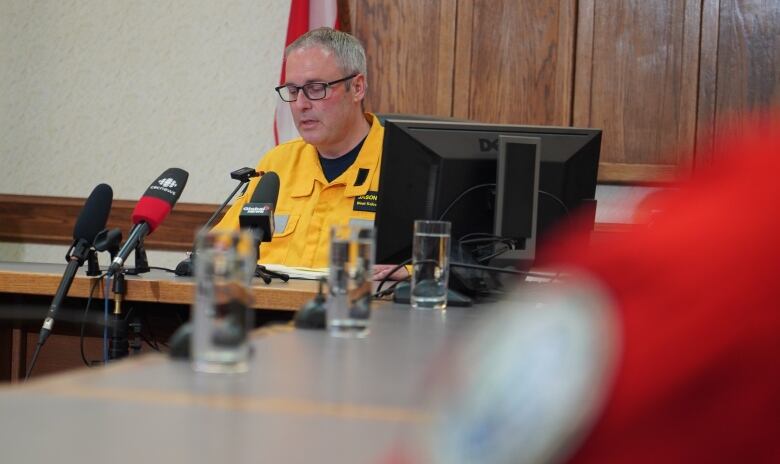 A man wearing a yellow uniform talks into multiple mics at a news conference.