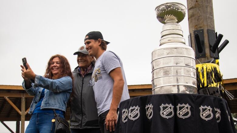 Three people take a selfie with the Stanley Cup.