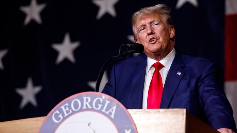 Donald Trump speaks at a podium with a Georgia sign on it. 