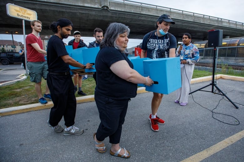 Transit users carry cardboard boxes painted blue to represent Line 3 in Scarborough on Aug. 23, 2023. 