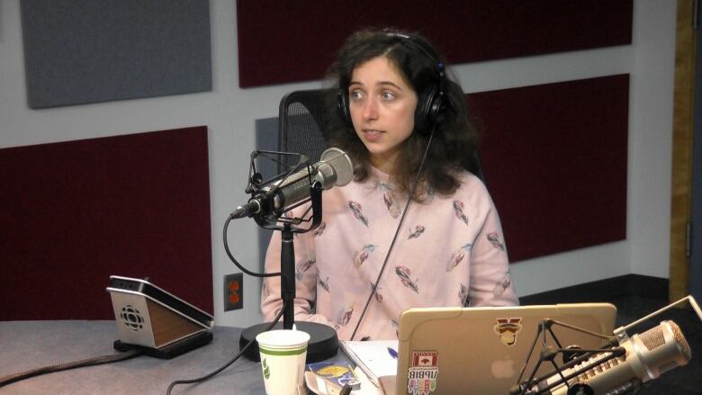 A woman with long black hair sits in front of a radio microphone.