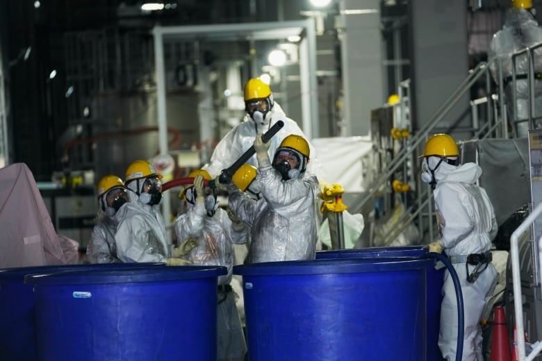 Men in hazmat suits work inside a facility with equipment to remove radioactive materials inside a plant.