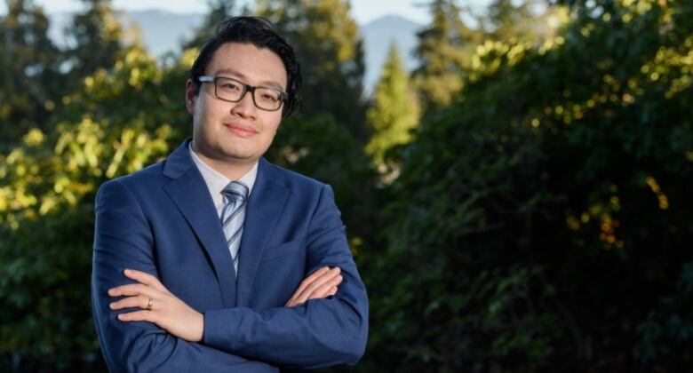 A lawyer poses with his arms crossed. Trees are in the background.