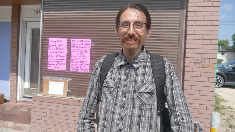 A man stands in front of two pink posters taped to a building.