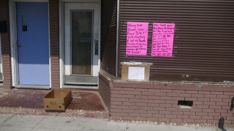 Two pink posters and a white sign are taped to a building.