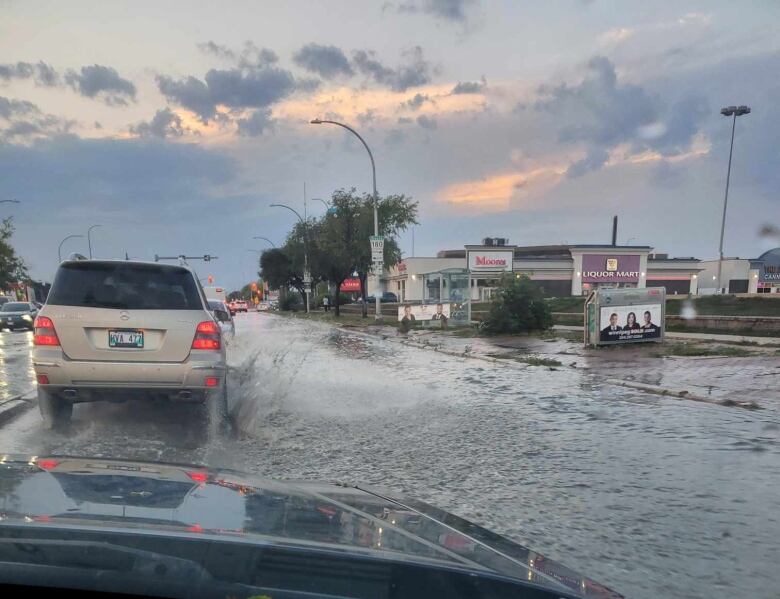 A car drives down a street flooded with water