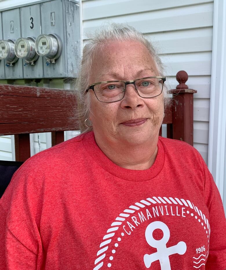 A woman in her 60s is wearing a read t-shirt. She is wearing glasses and her grey hair is in a braid.