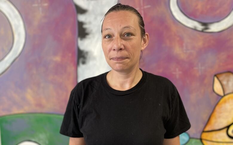 A woman in a black t-shirt with her hair pulled back standing in front of a mural