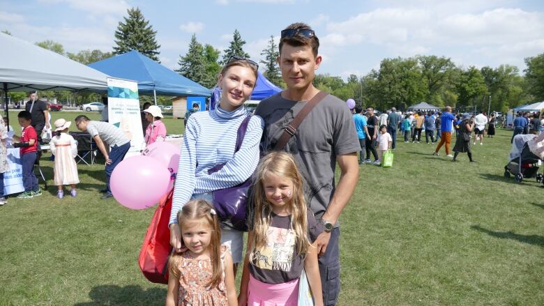 A man stands next to a woman behind their two young daughters.