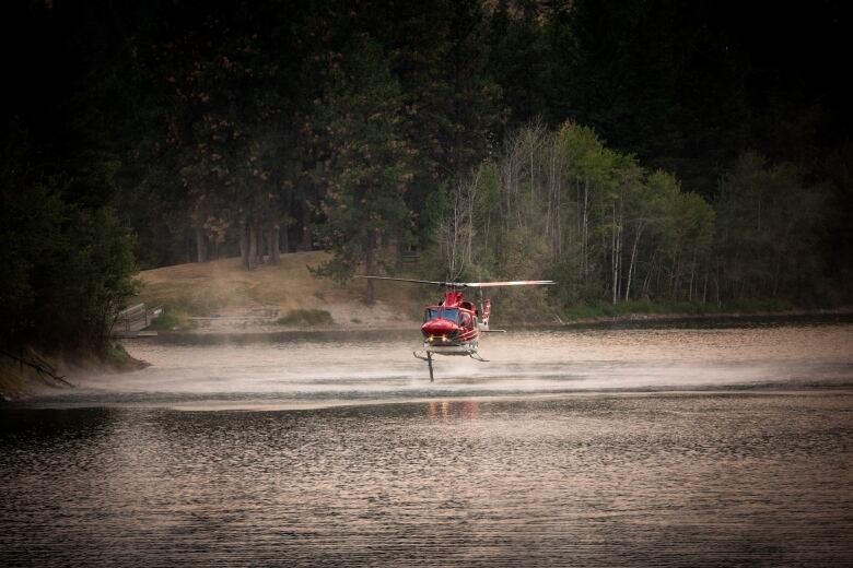 A red helicopter picks up water from a lake.