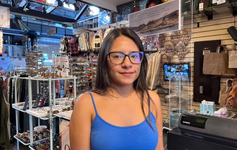 A woman wearing glasses and a blue tank top poses in a store.