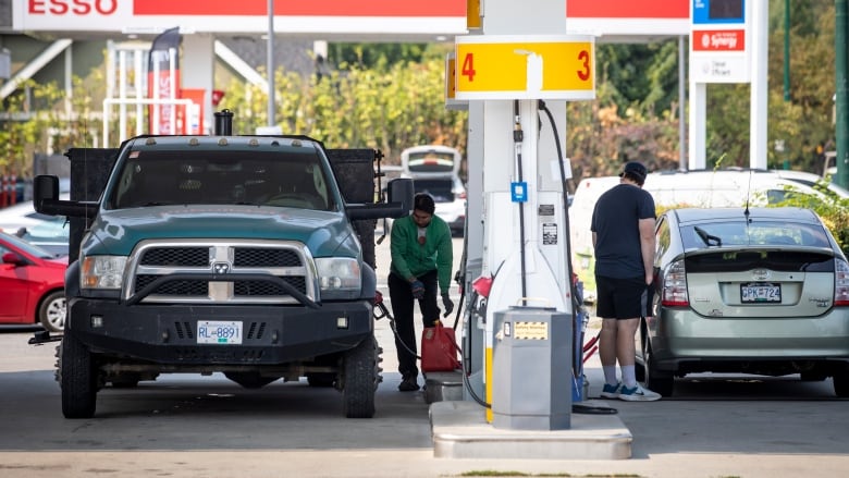 Two people at the pumps filling up at a gas station.