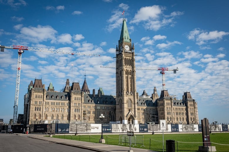 A legislature and its lawn on a sunny summer day. There are construction cranes behind it.