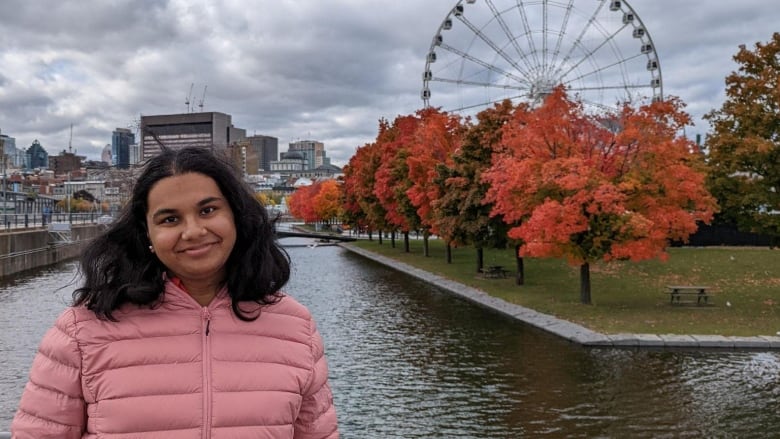 A woman stands by water and a Ferris wheel.