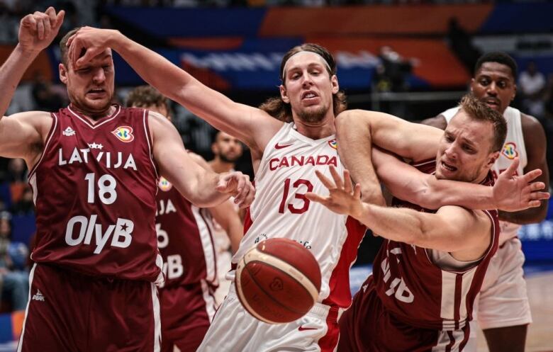 Three basketball players fight for a loose ball.