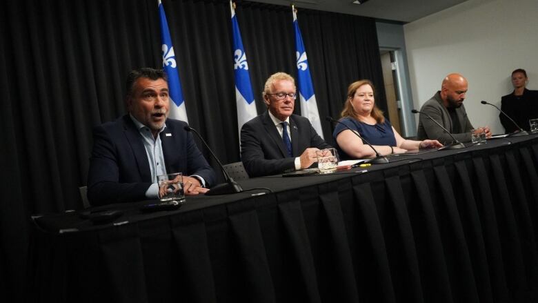 People sit a table in front of a series of Quebec 