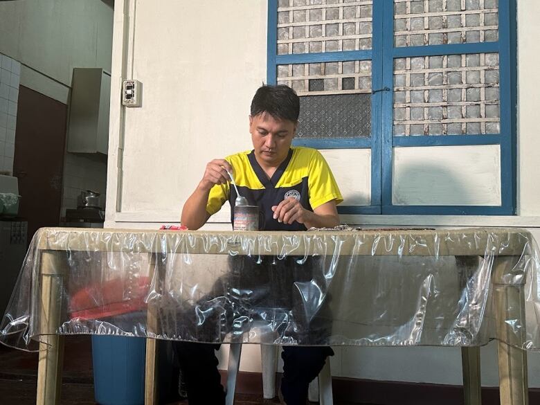 A man in yellow and blue scrubs stirs a spoon in a mug.