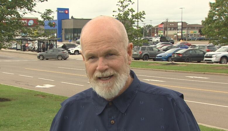 Bald man with beard speaks in a parking lot. 