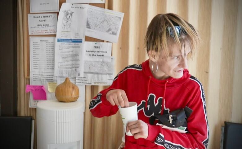 A woman with short hair and wearing a red sweatshirt reaches into a cup.