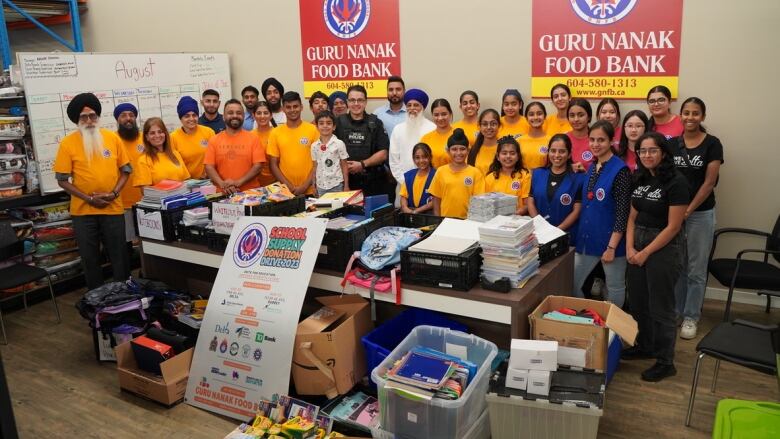 About 30 people, mostly Sikh youth, gather around a table displaying collected donations of school supplies.