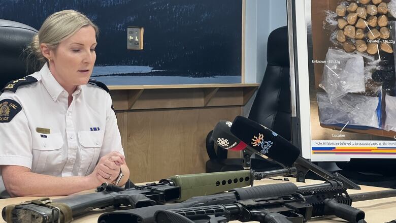 A female RCMP officer sits behind a table where several firearms are laid out.