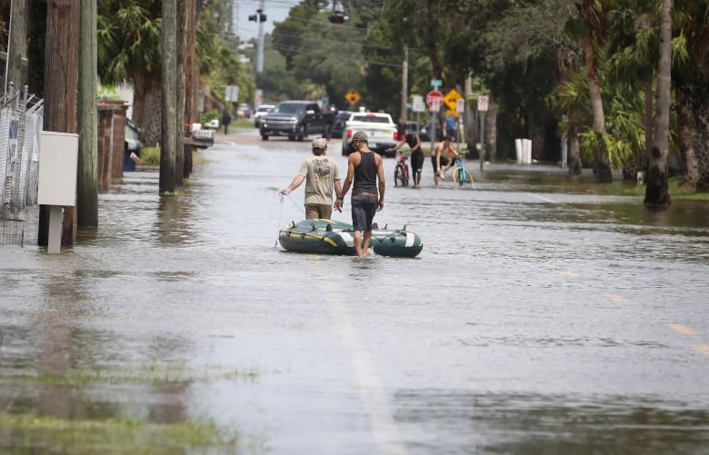 People walking down a flooded street, pulling a rubber raft