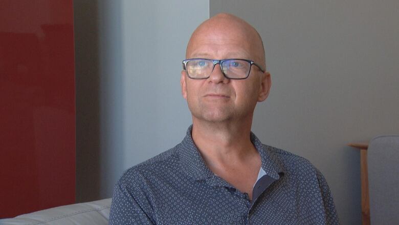 A man with glasses sits on a couch.