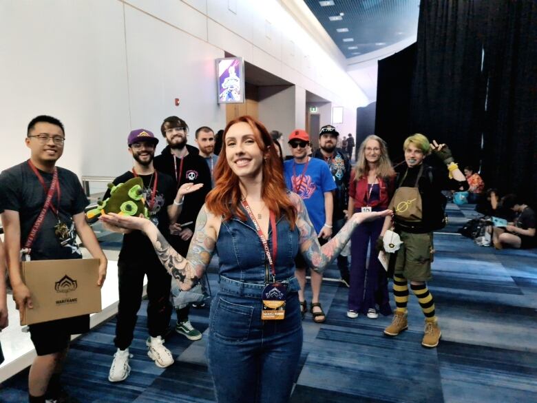 A woman with red hair poses with fans in the background at a convention hall.