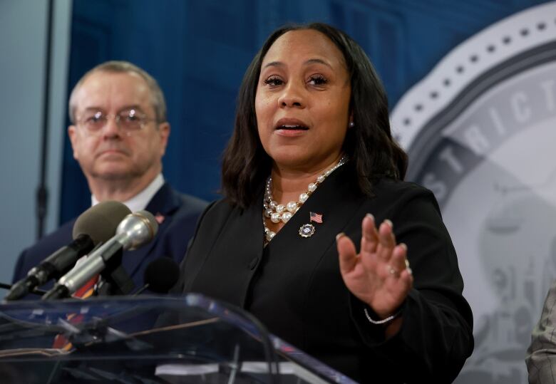 A woman in professional attire is shown speaking at a podium.