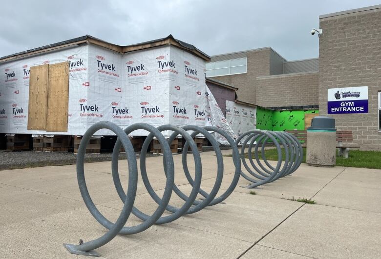 A spiral bike rack in the foreground with structure in the background with exposed plywood and white Tyvek wrap. 