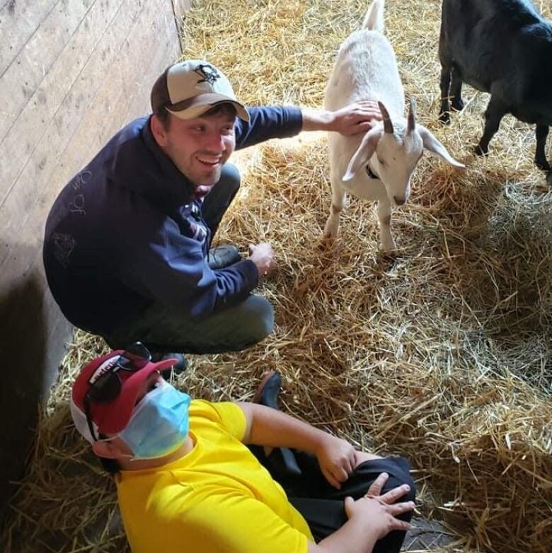 two young men in barn with black goat and white goat