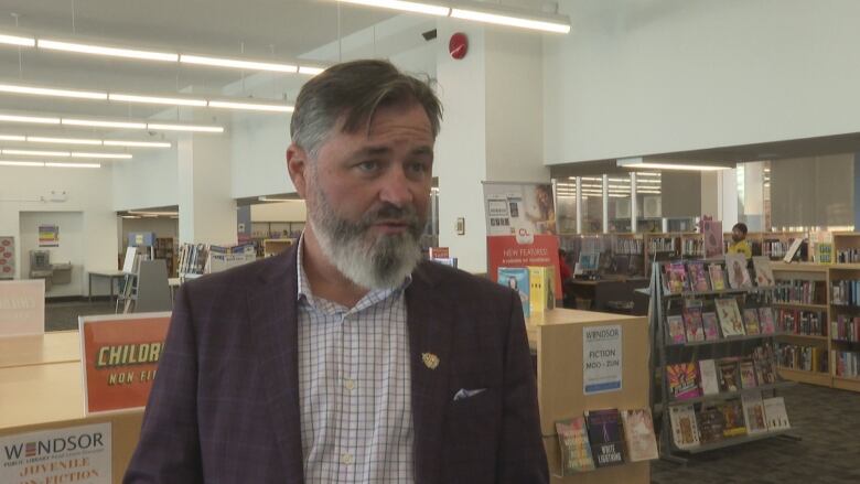 A bearded man in a library during the day.