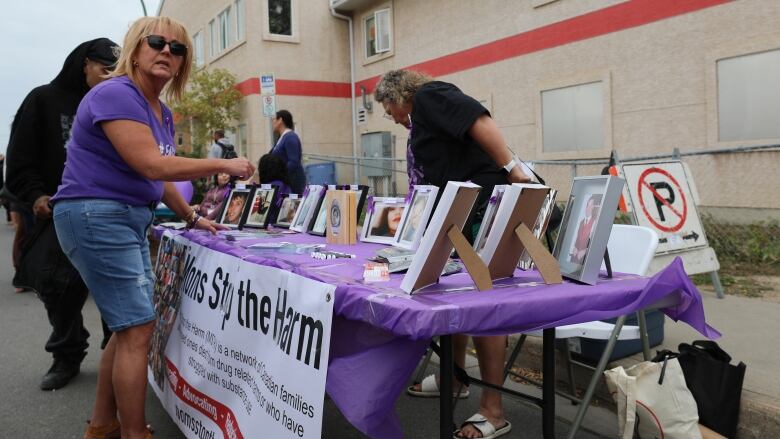 A woman in a purple shirt organizes photographs and pamphlets on a table. 