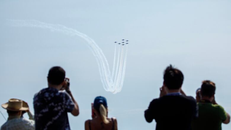 Five spectators watching the Snowbirds practising by a lake.