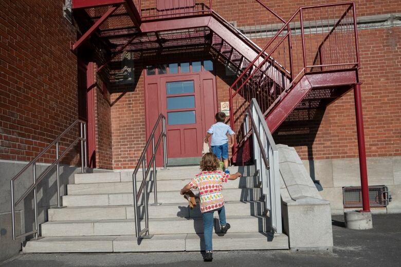 Kids walk up a staircase into a brick building.