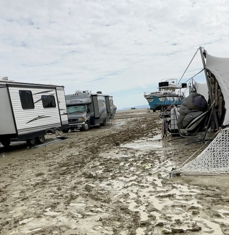 Recreational vehicle and tents are seen on a muddy site.