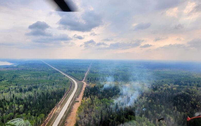 Aerial shot with a rural road surround by forest - the forest on the right side of the road is smoking.